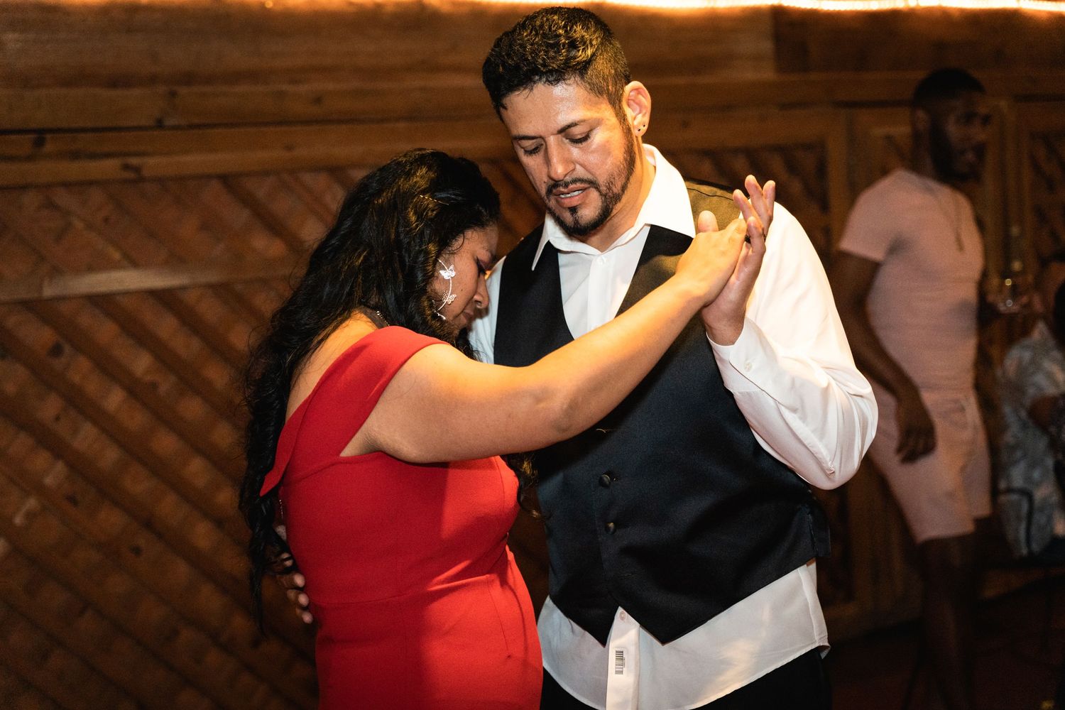 A couple dances together at a reception, with the person in red wearing a striking dress.
