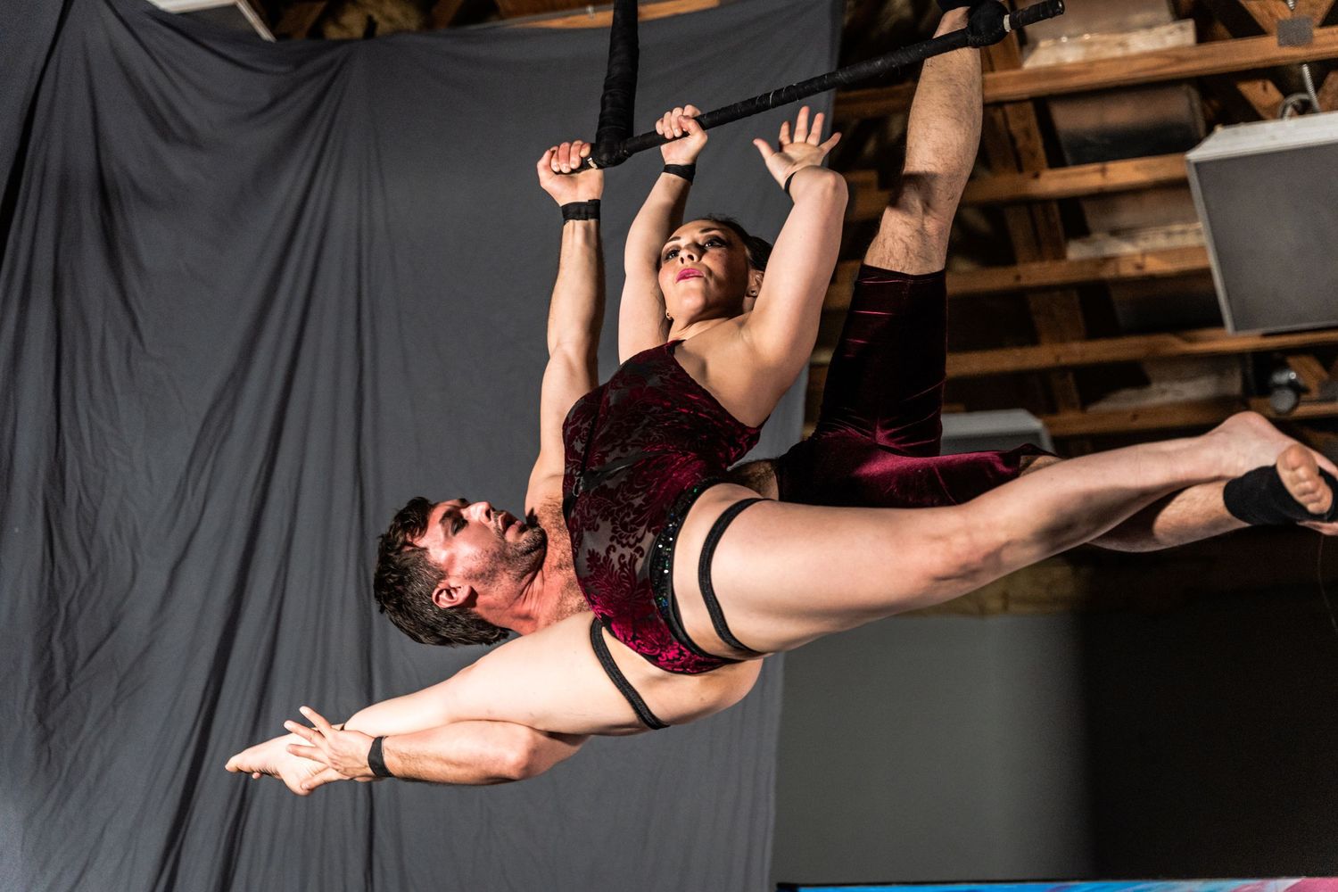 Two aerial performers in burgundy costumes execute a dramatic suspended pose during a dance routine.