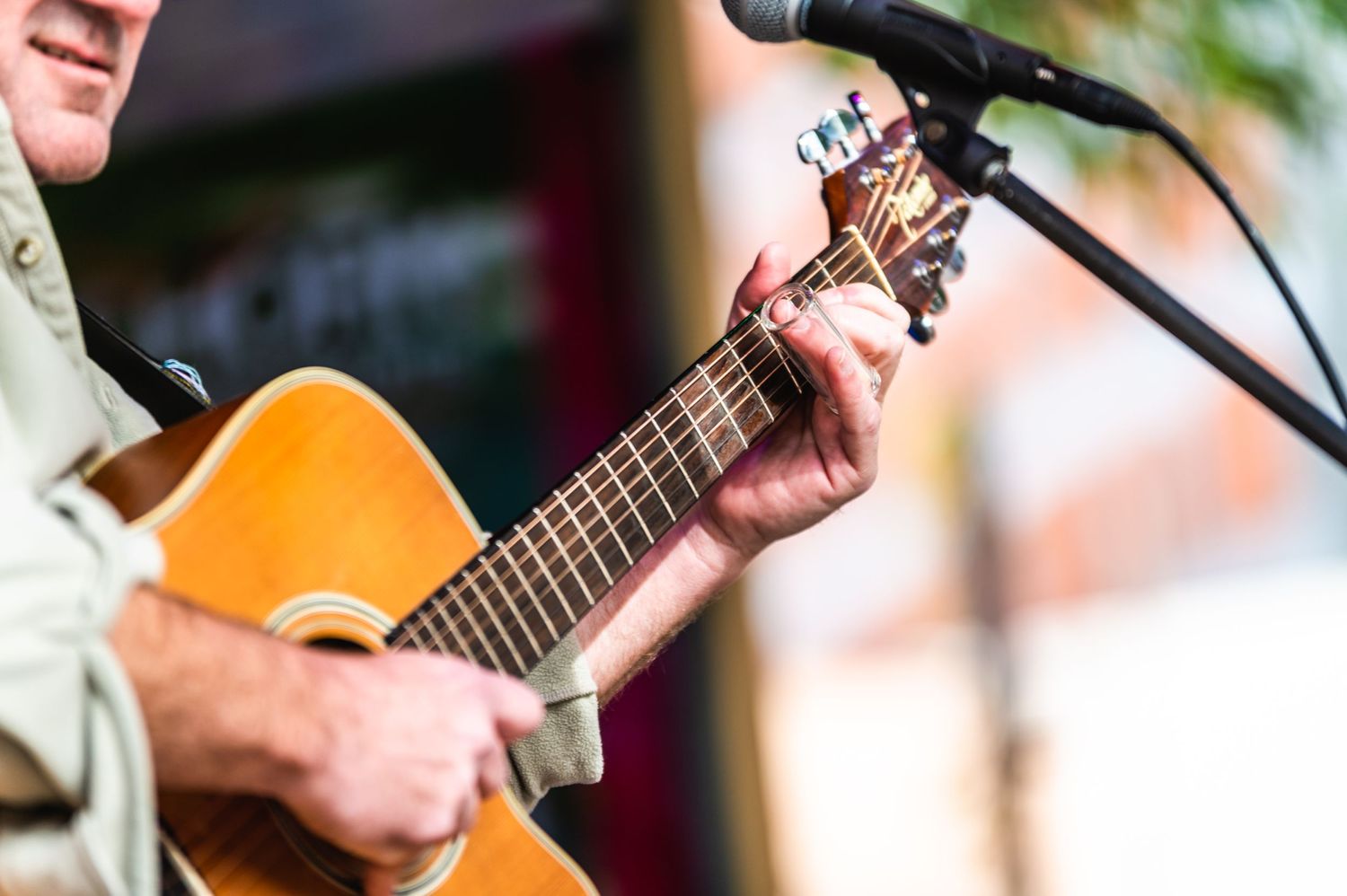 Close-up shot of hands playing an acoustic guitar with a microphone in frame.