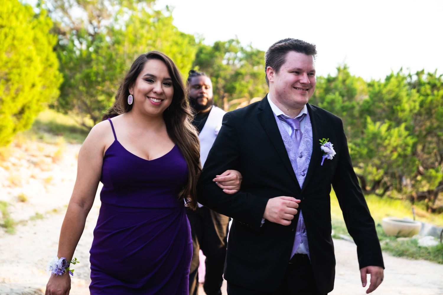 Wedding party members walking together outdoors in purple and formal attire.