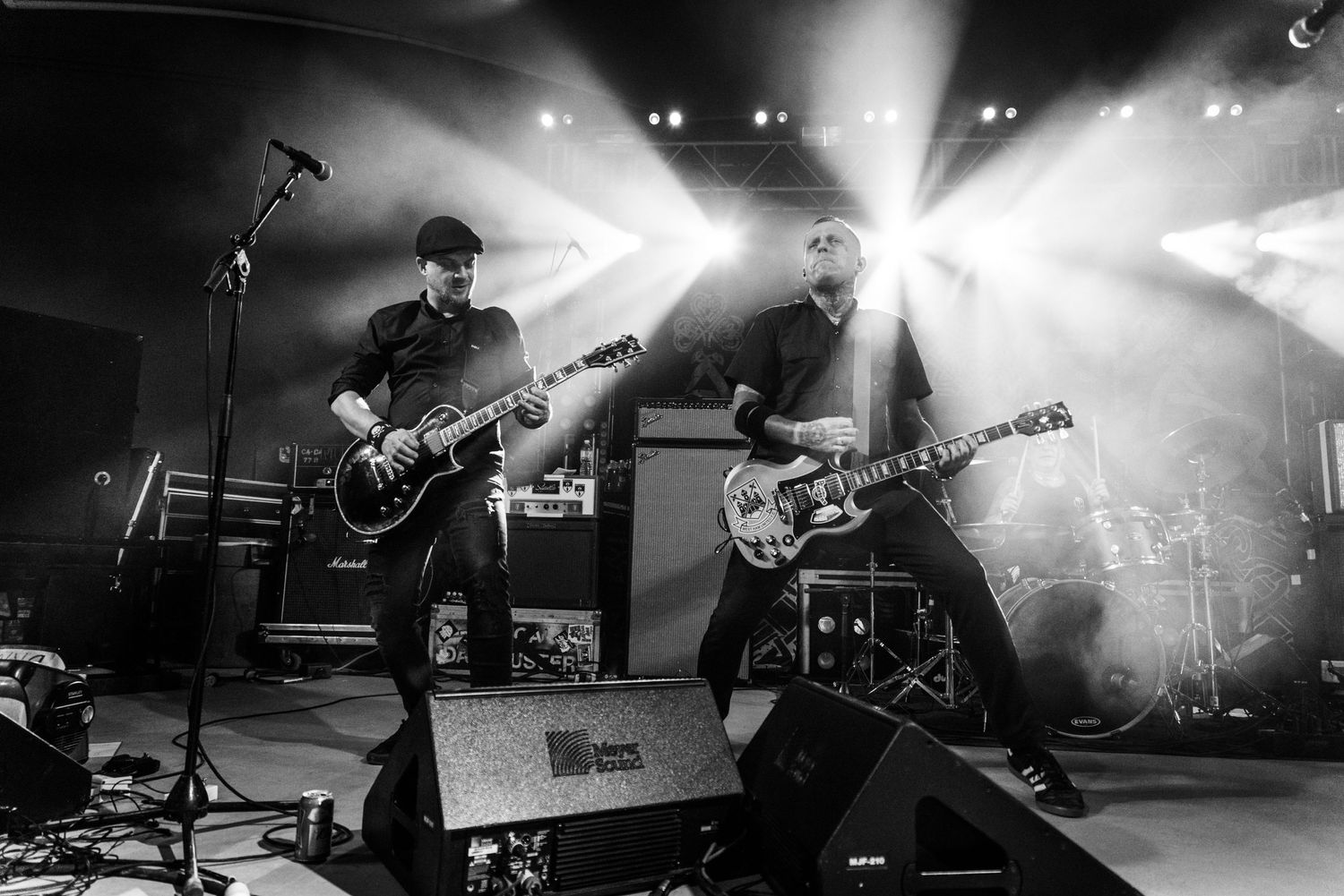 Black and white photo of band members playing guitars on illuminated concert stage.