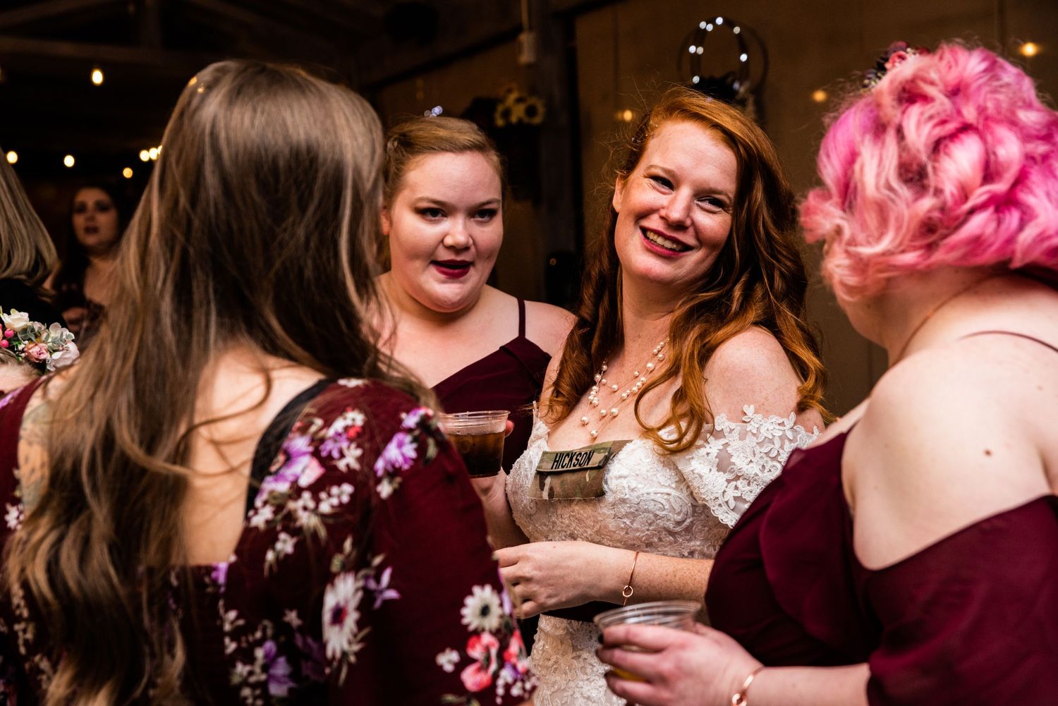 Wedding party members in burgundy dresses share laughter during reception festivities.