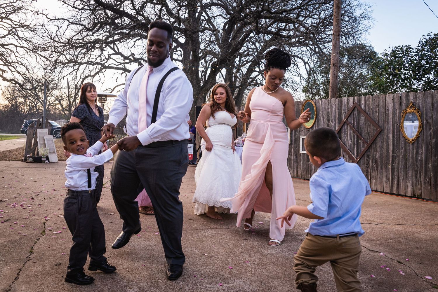 Joyful dancing scene at an outdoor wedding reception with family members and children.