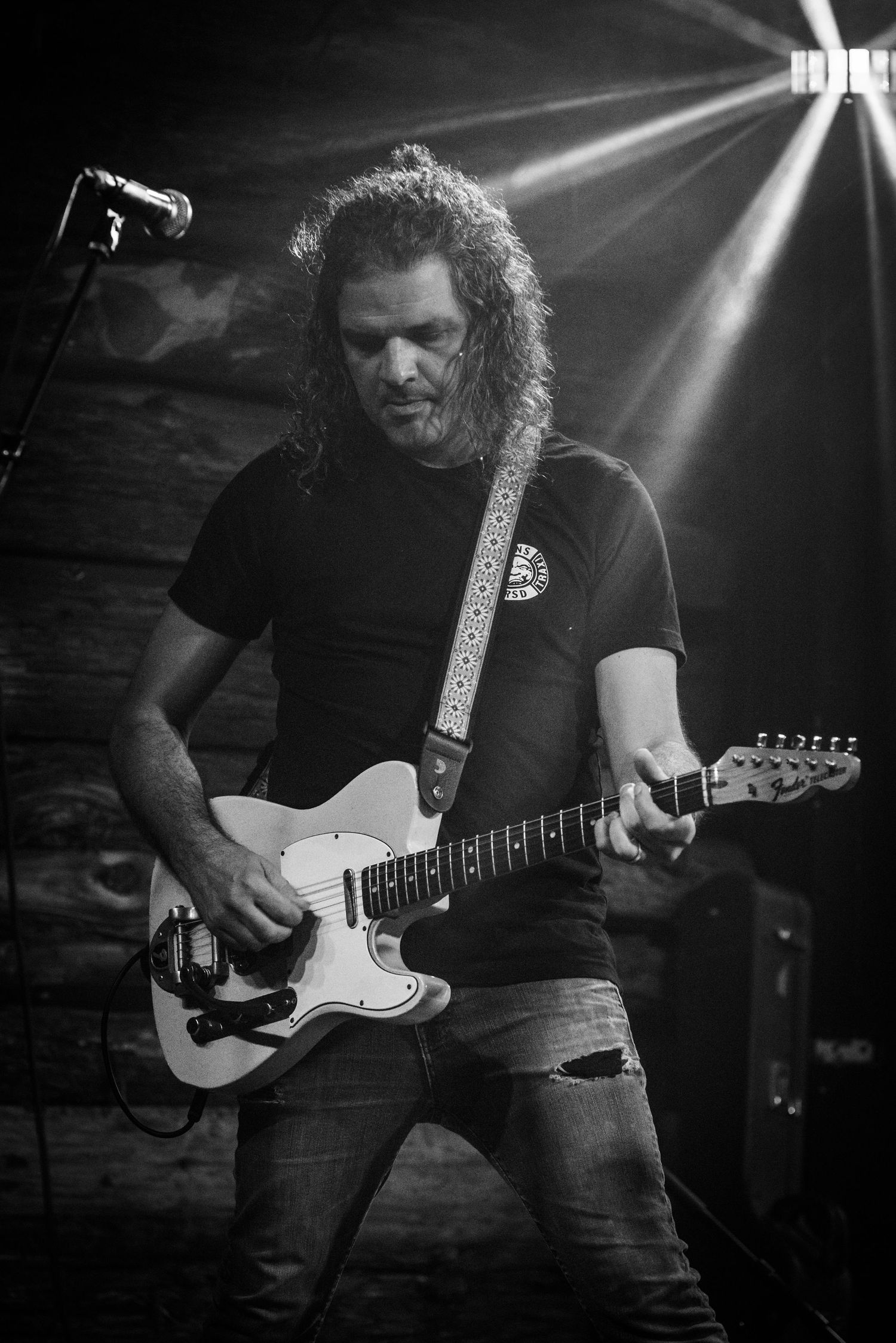 A rock guitarist performs on stage with a white electric guitar under dramatic stage lighting.