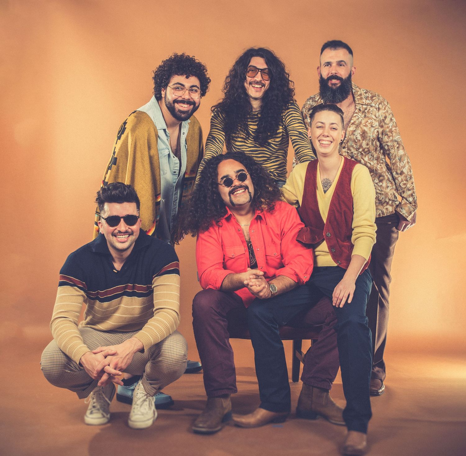 Group photo of band members in retro-styled clothing posing against orange backdrop.