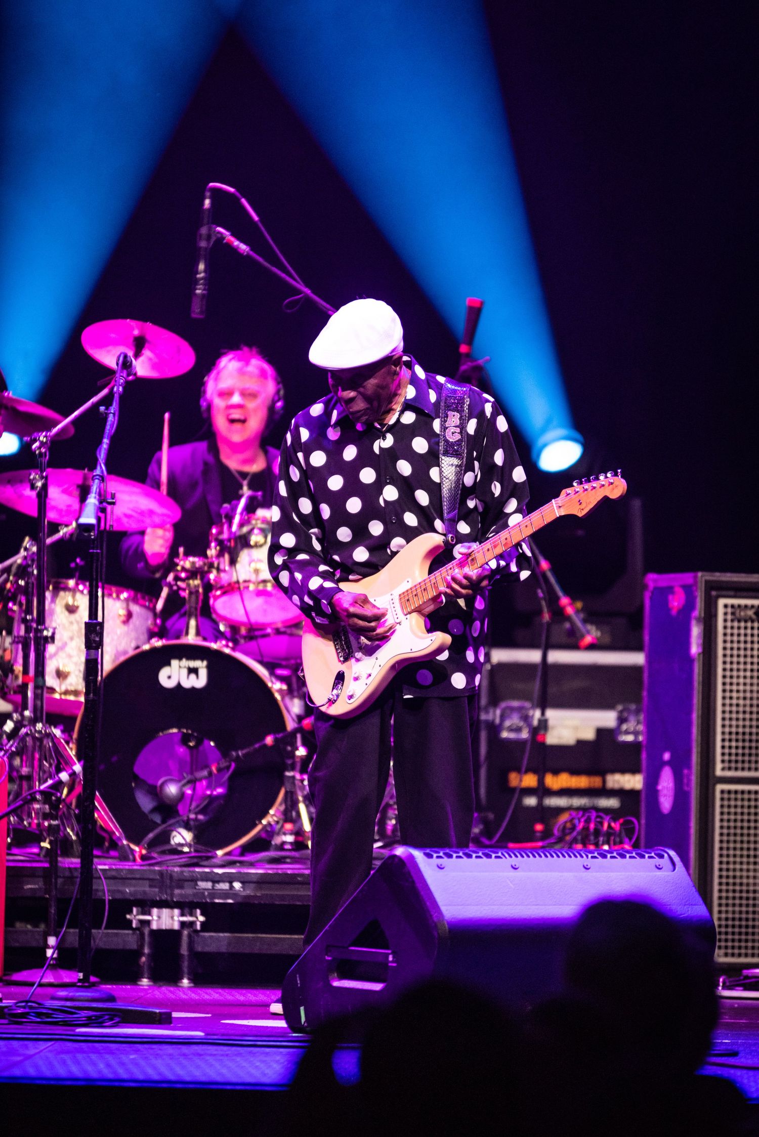 Rock band performs on concert stage with dramatic blue and purple lighting effects.