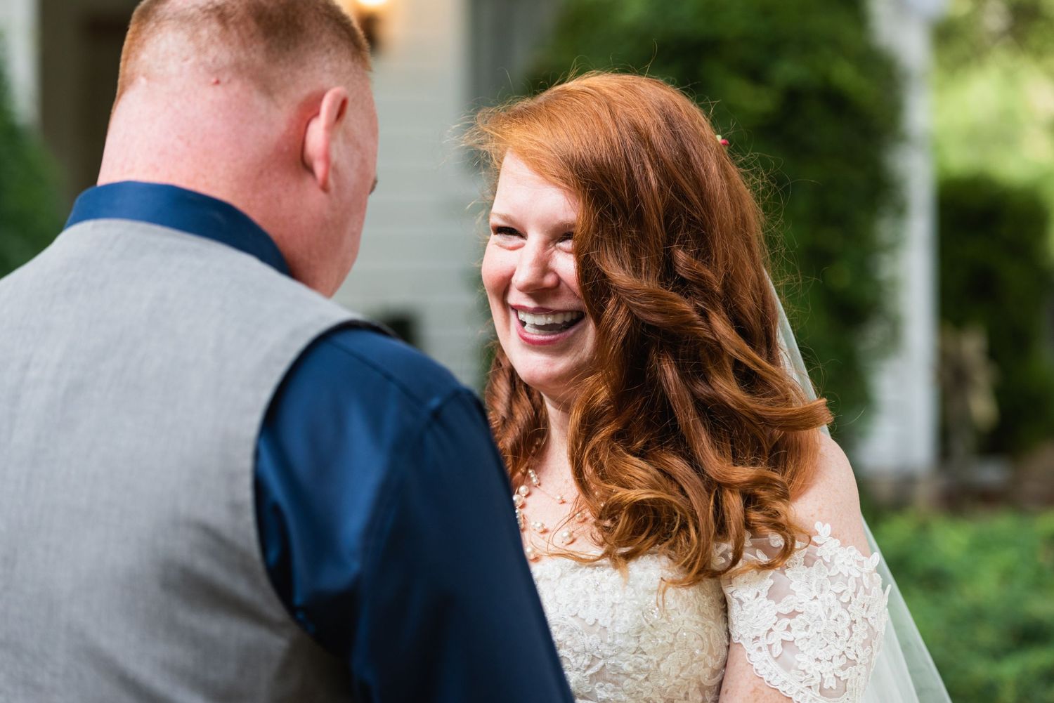 A joyful bride in a lace dress shares a heartfelt moment with her groom outdoors.
