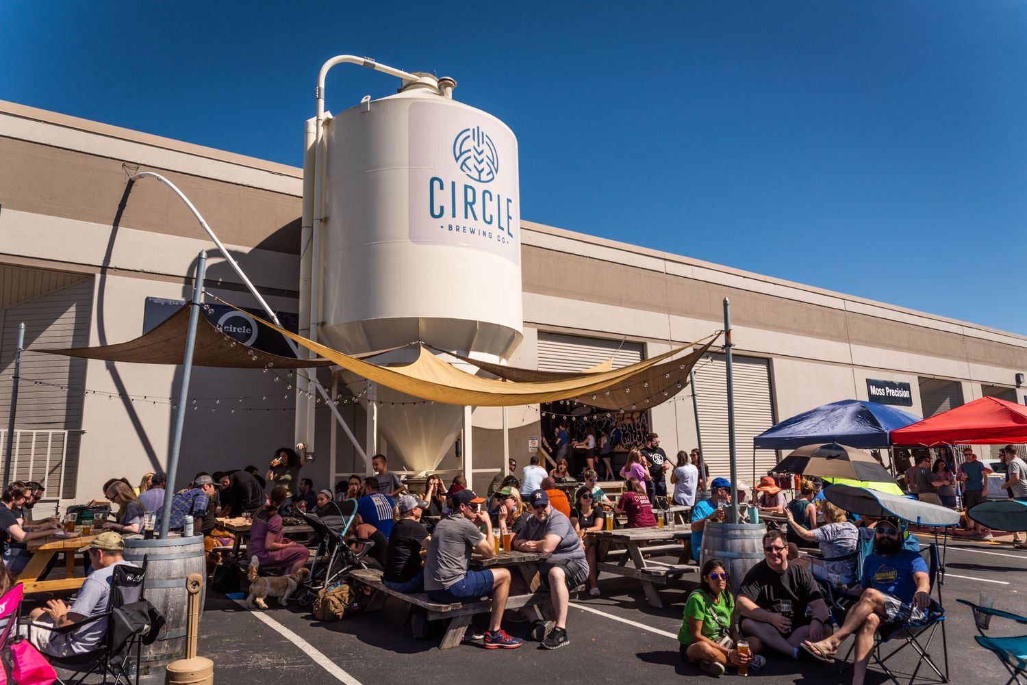 Large brewery tank with outdoor seating area under blue sky.