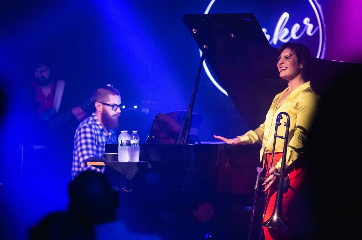 Musicians perform under blue stage lights with a piano and neon Parker Jazz Club sign visible.