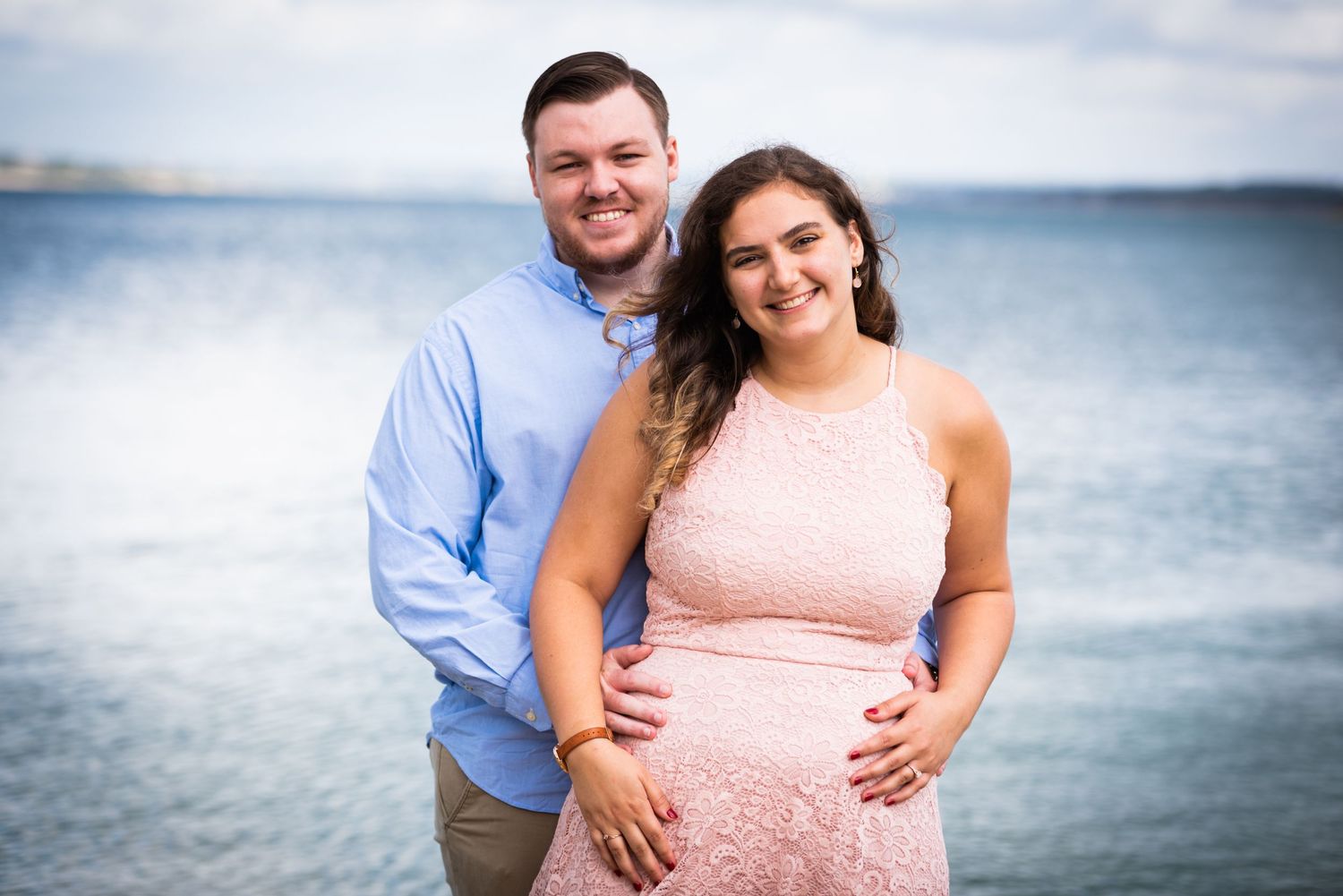 A happy couple poses for a portrait by the ocean on a cloudy day.