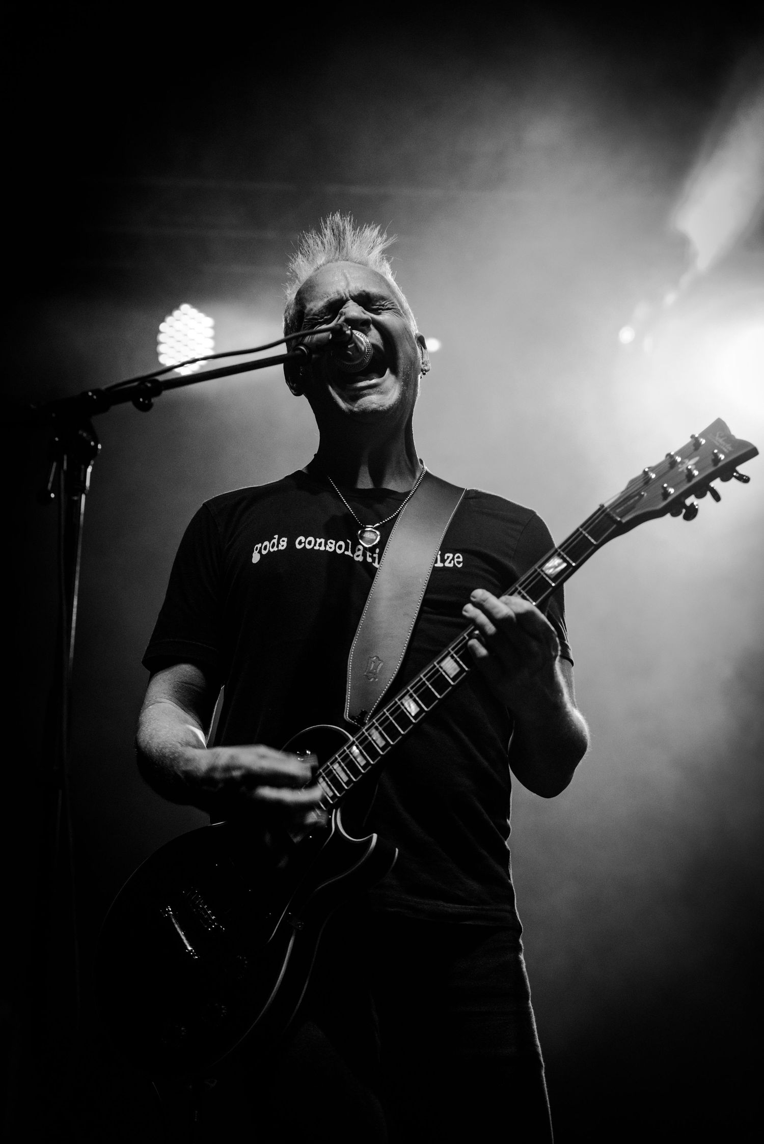 Black and white concert photo of a guitarist performing on stage with dramatic lighting and fog effects.