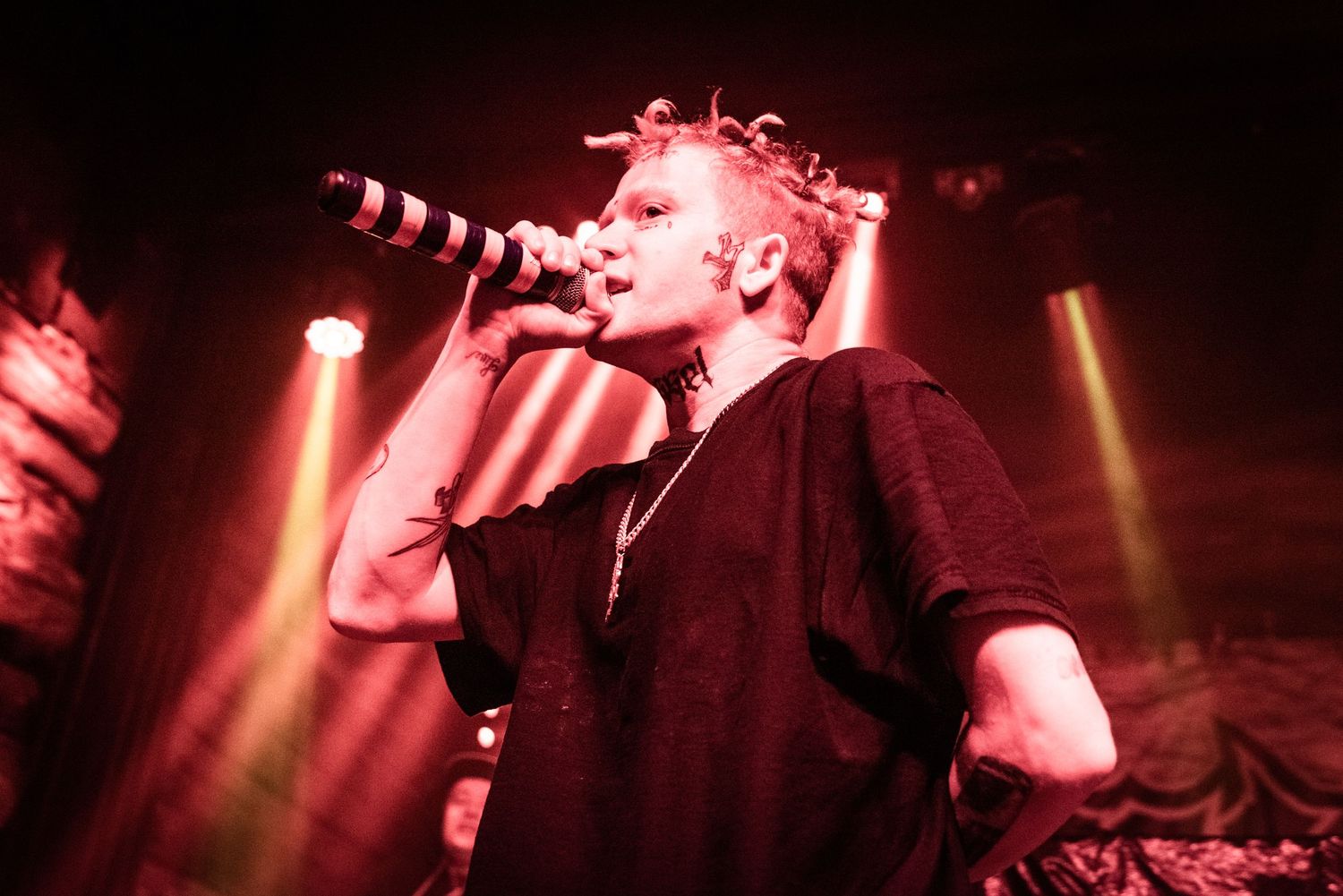 A performer sings passionately on stage under dramatic red lighting during a concert performance.