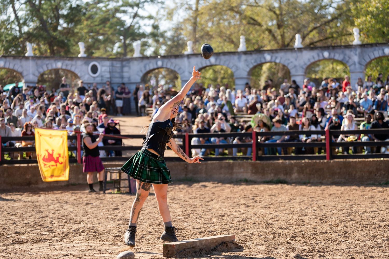 Medieval knights in armor engage in a tournament battle at a Renaissance festival while spectators watch from bleachers.