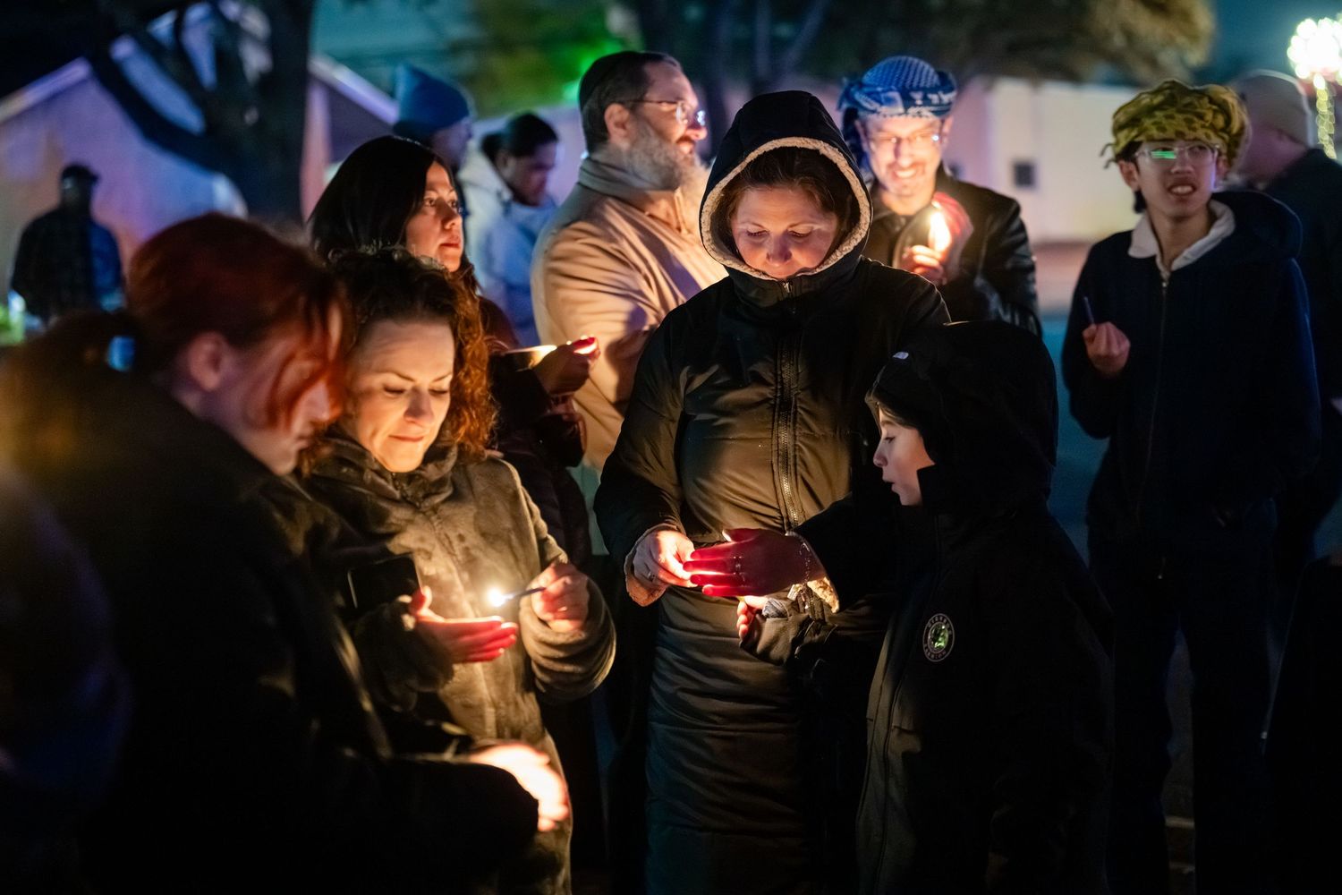 A group of people hold candles during a nighttime vigil gathering in darkness.