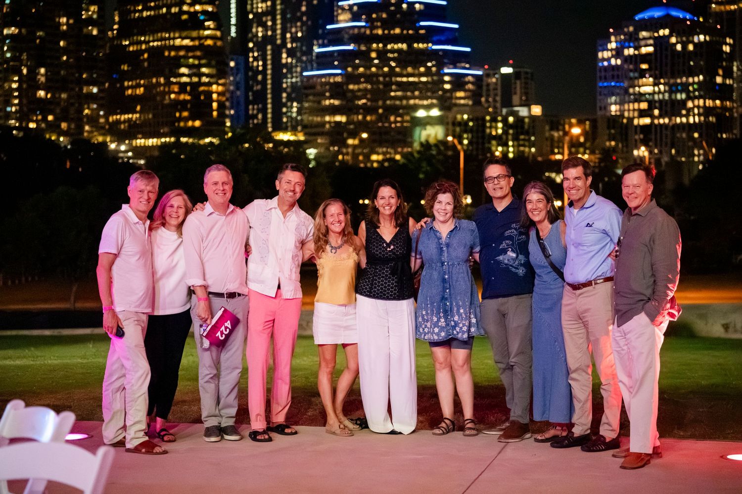 Wedding party poses for photos at night with city skyline illuminated in the background.
