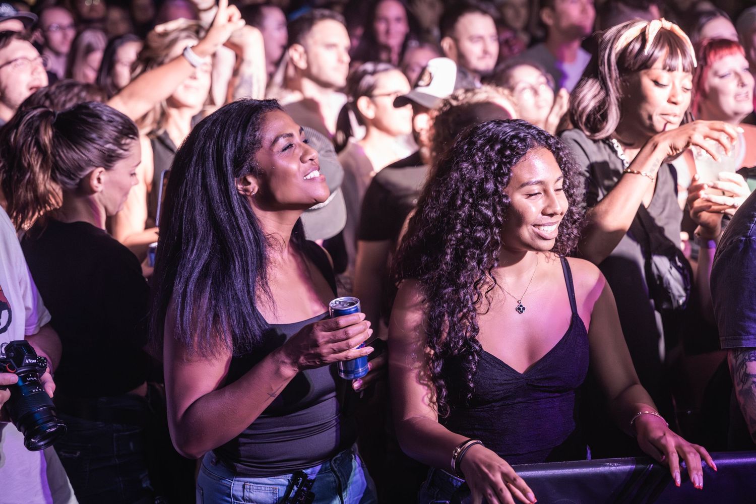 Concert audience members dance and sing along enthusiastically at a live music performance in a crowded venue.