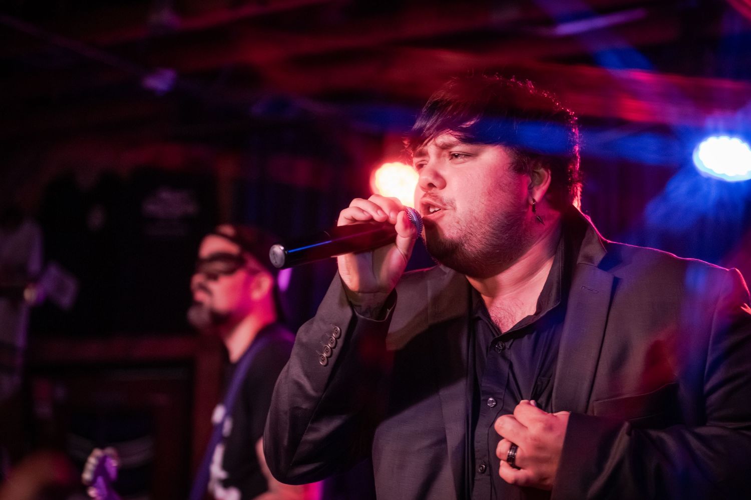 Musicians perform on stage in a dark venue with blue and purple lighting creating a moody atmosphere.