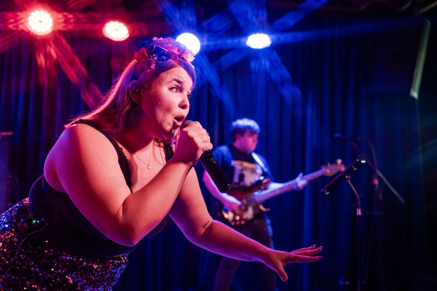 A performer sings passionately on stage with dramatic red and blue concert lighting creating a moody atmosphere.