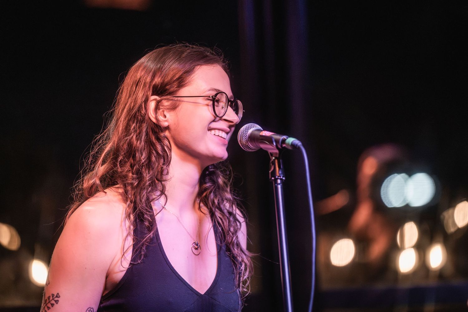 A performer with glasses sings passionately into a microphone on stage under warm lighting.