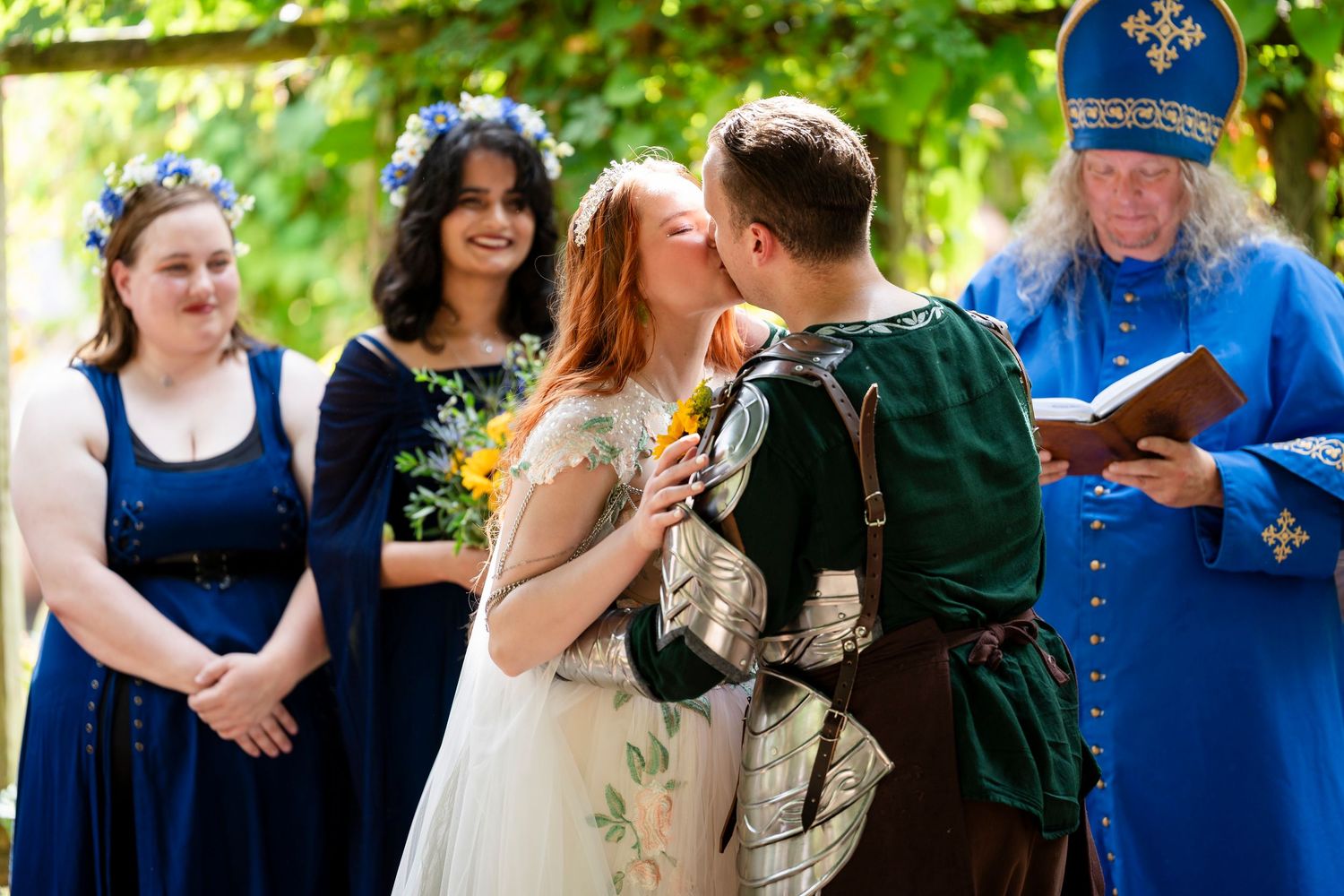 An outdoor wedding ceremony with attendants in blue dresses and an officiant in blue robes during a romantic moment.