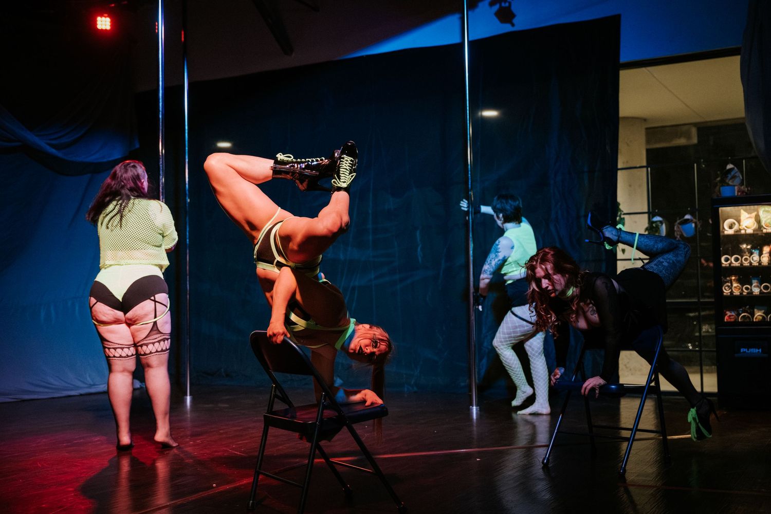 Performers on stage with pole dancing acts under blue lighting in a dark venue.