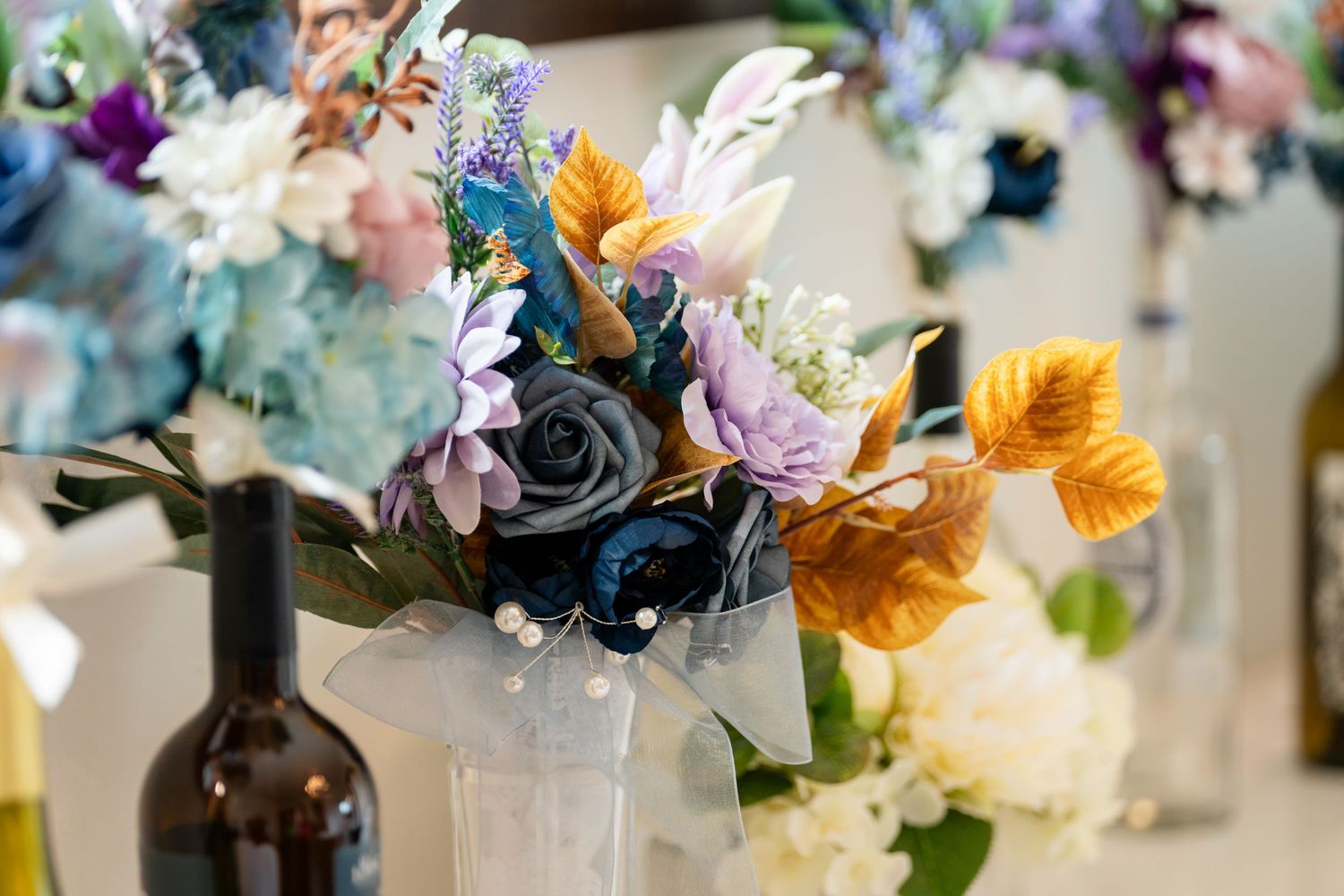 Colorful artificial flower bouquets with blue, purple, and gold blooms arranged in glass vases on a decorated table.