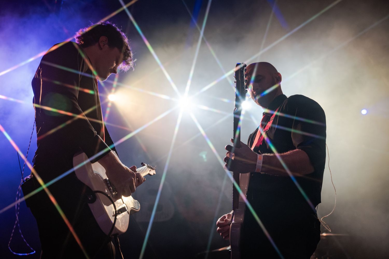 Two guitarists performing on stage with dramatic laser lights and smoke at a live concert.