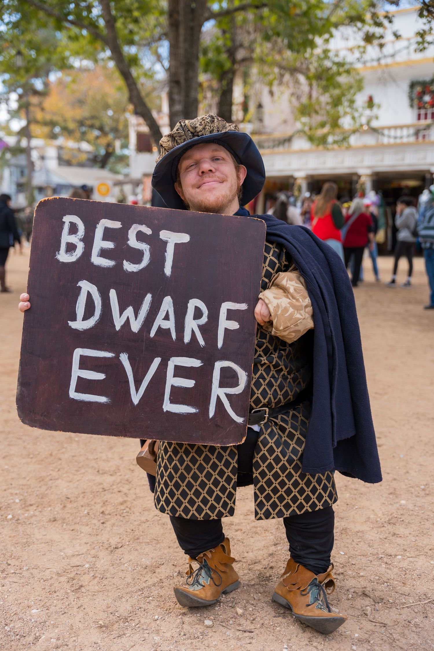 A series of signs on a dirt ground spell out 'BEST DWARF EVER' with medieval-style clothing and boots visible.