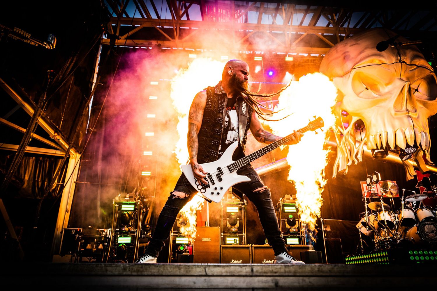 A dramatic pyrotechnic display illuminates a stage during a rock concert performance with flames and smoke effects.