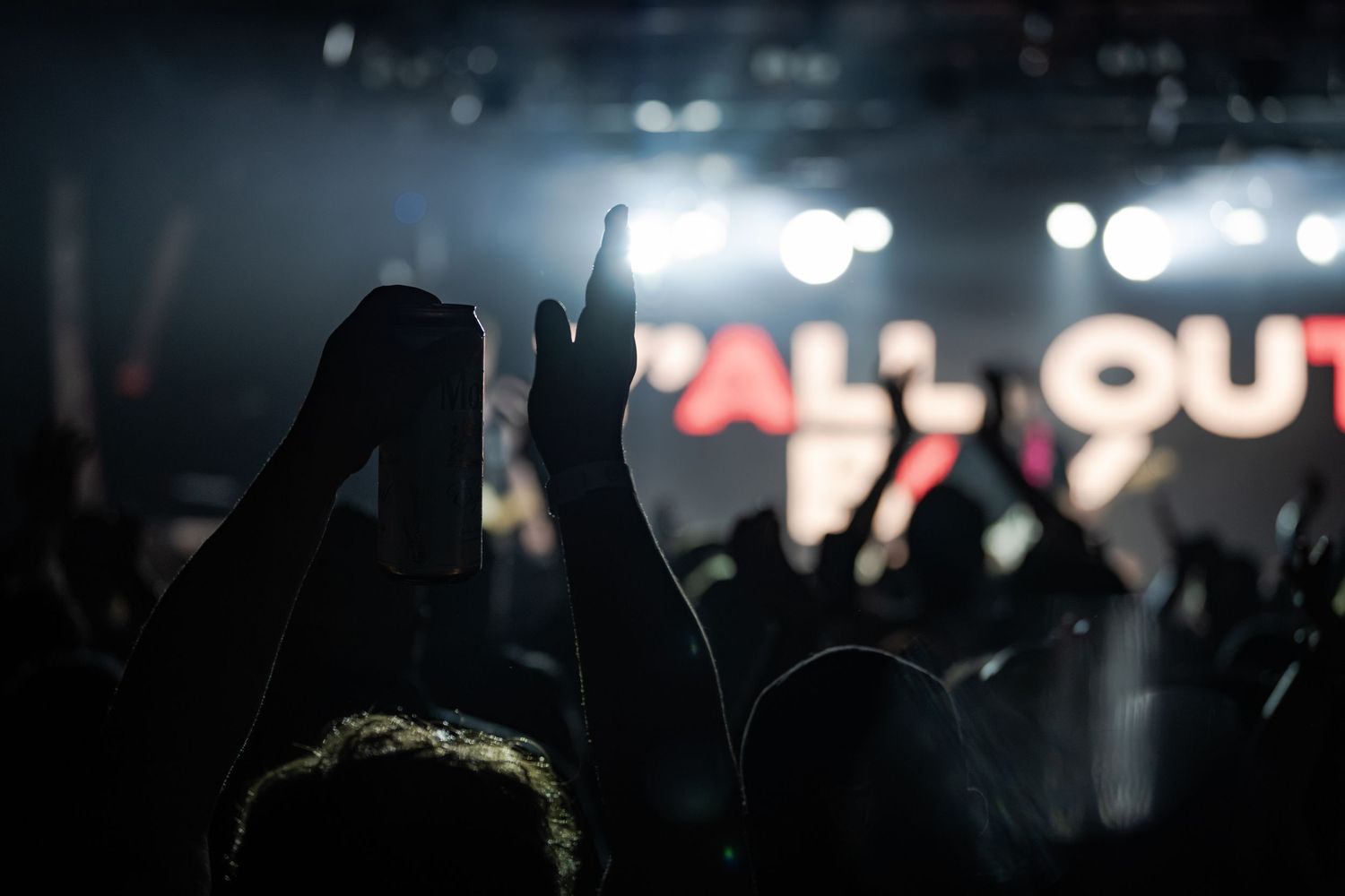 Crowd with raised hands at a Fall Out Boy concert with bright stage lights illuminating the dark venue.