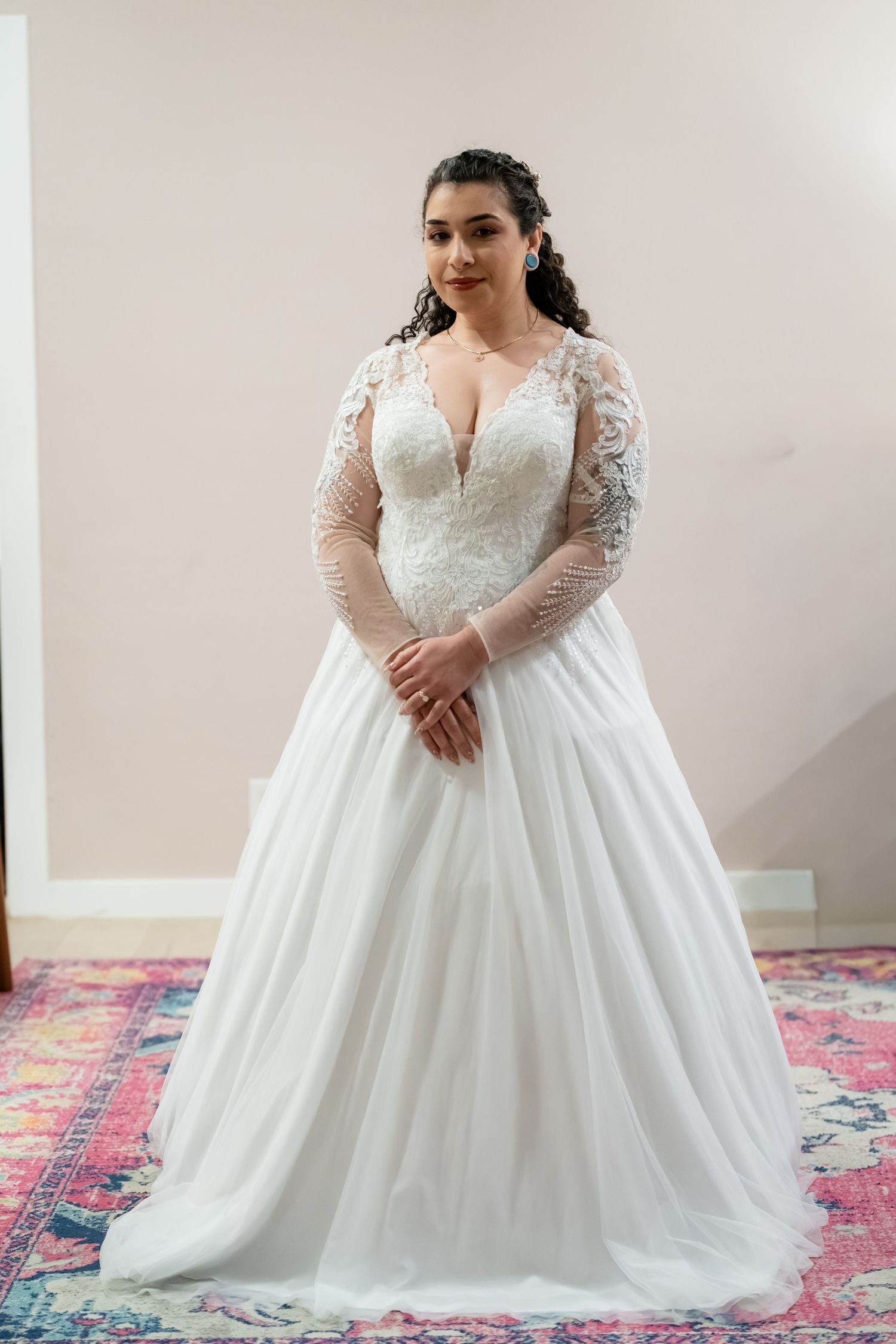 Plus-size bride wearing a long-sleeve lace ballgown wedding dress with deep V-neckline and flowing tulle skirt.