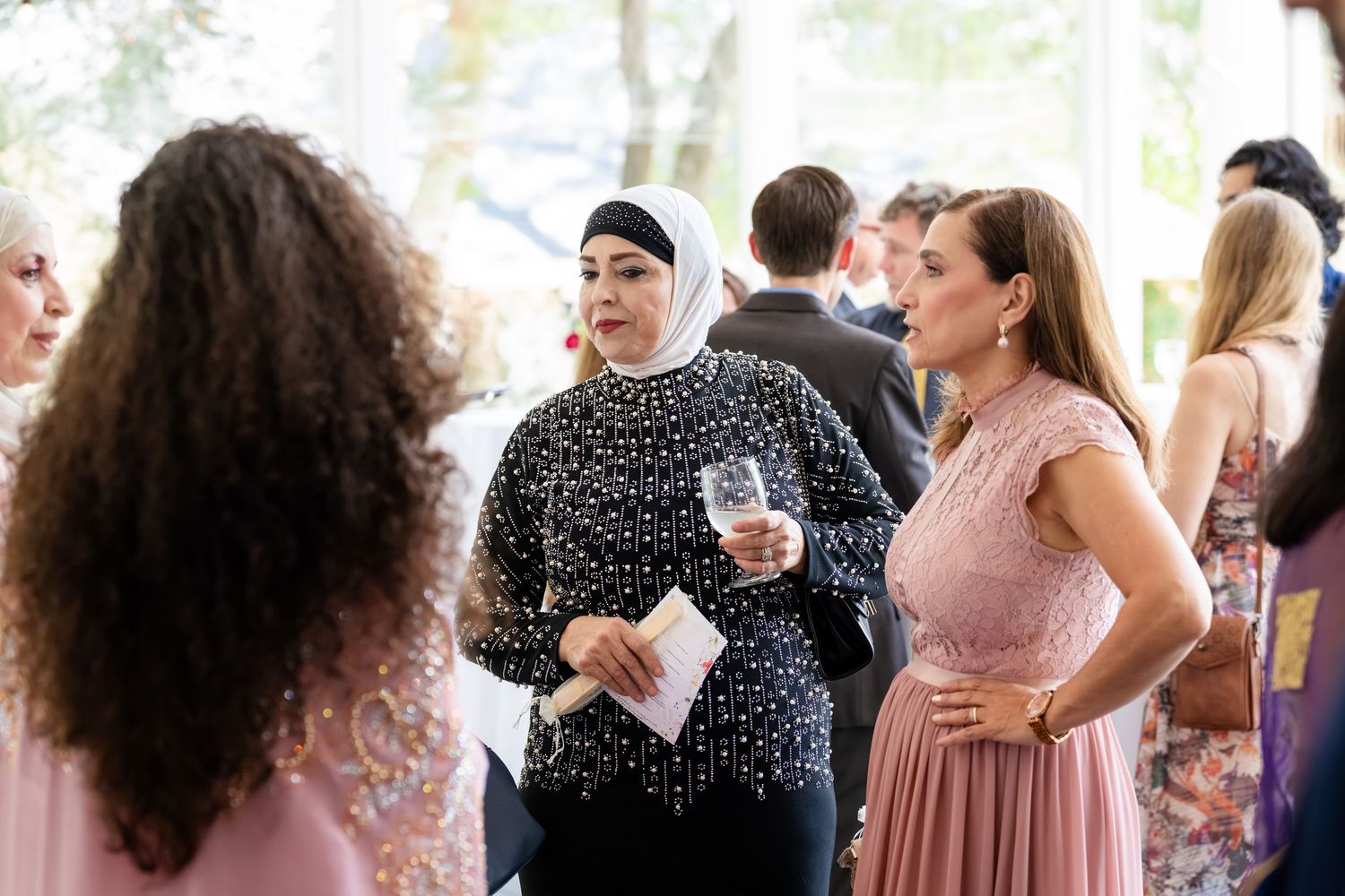 Elegantly dressed women networking at a formal event, one wearing a hijab and holding a glass.