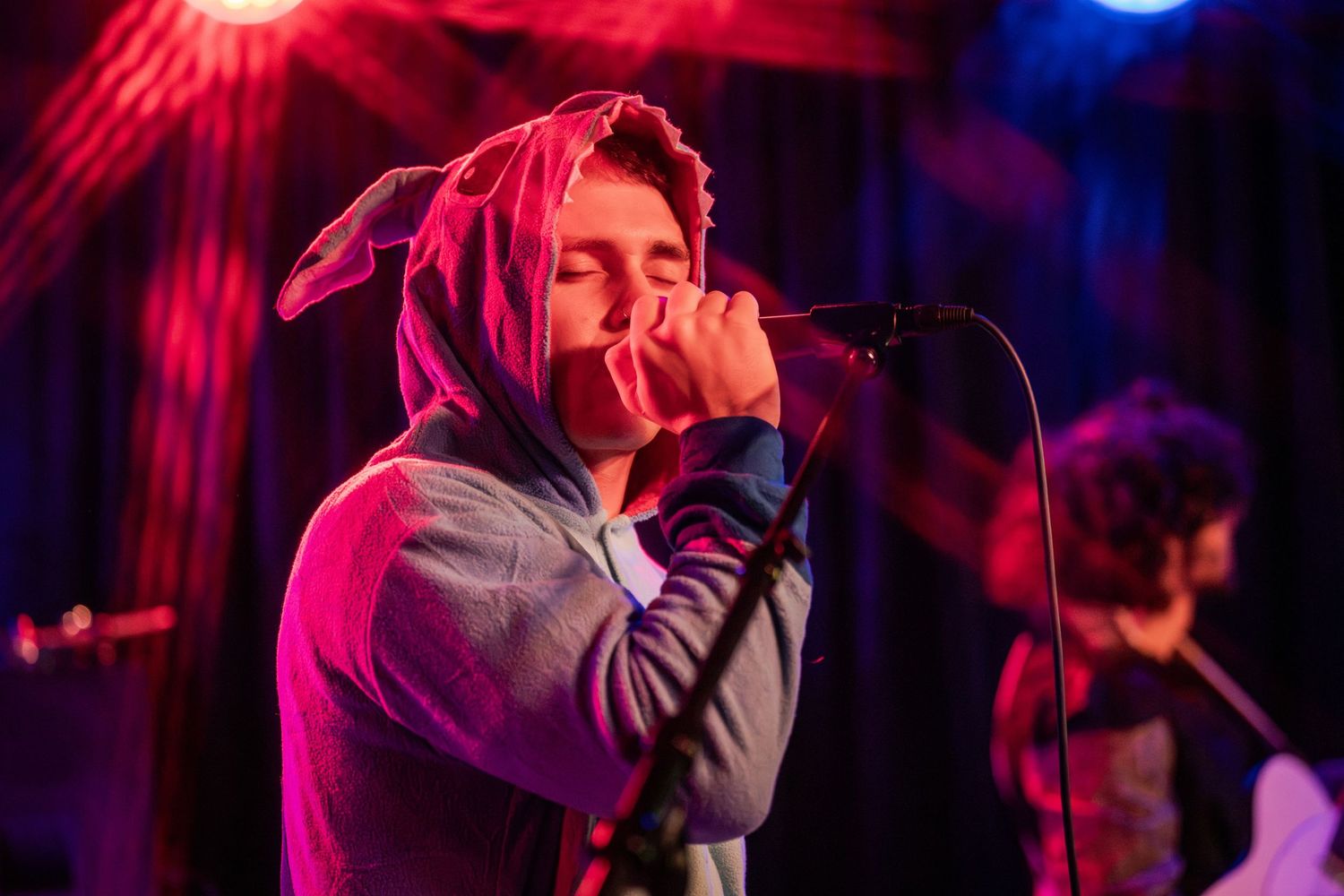 Concert performer sings passionately on stage with dramatic red and blue lighting in the background.