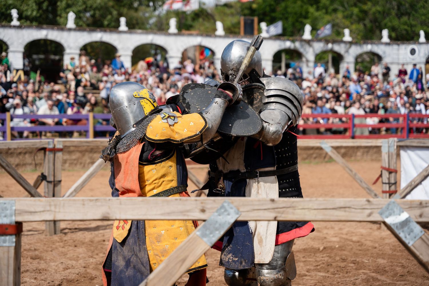 Two medieval knights in armor clash with swords during a historical reenactment battle at a renaissance fair.
