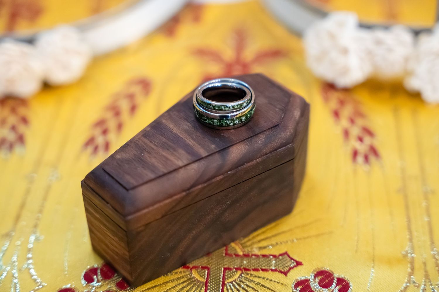 A handmade wooden ring box with dark wood grain sits on a yellow floral surface.