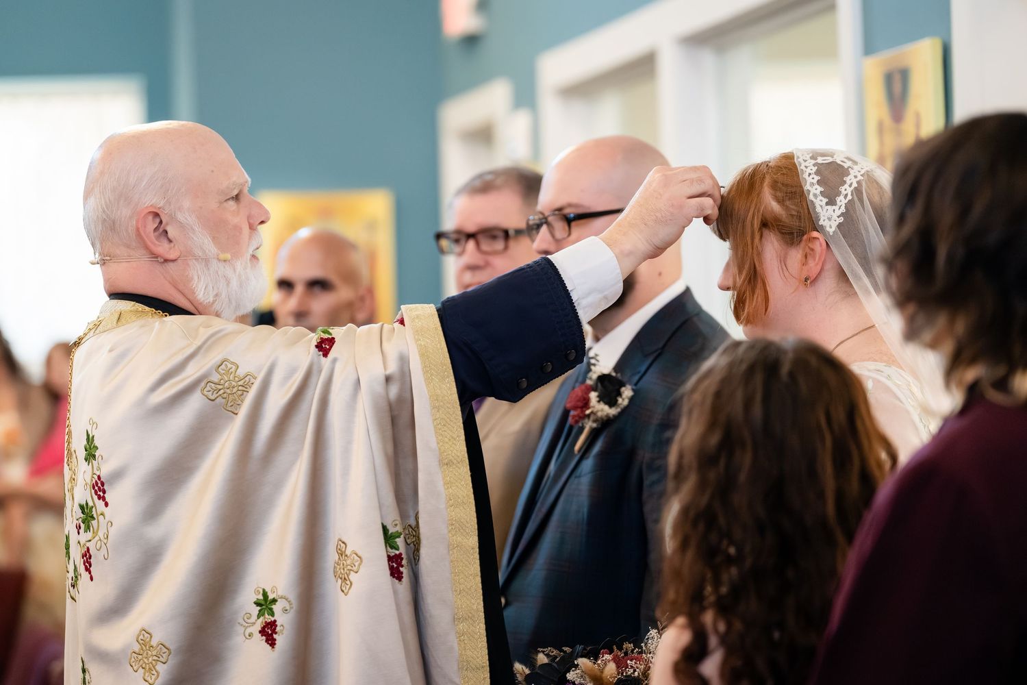 A group of people gather together during a wedding ceremony in a room with teal walls.