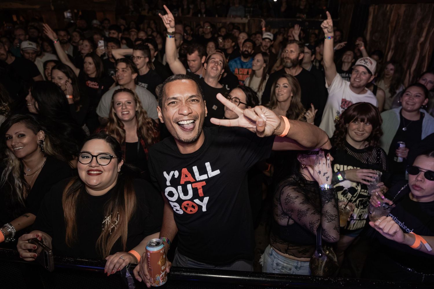 Excited concert crowd with people making peace signs and cheering at a live music event.