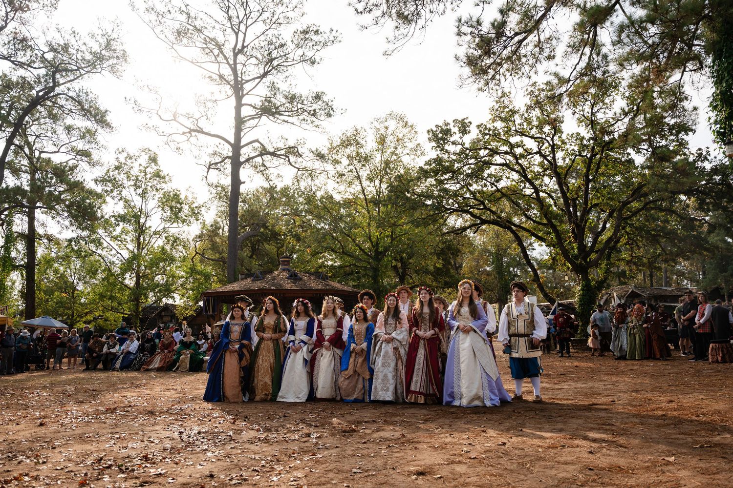 Wedding party in formal attire poses together for group photos in a scenic outdoor garden setting at sunset.