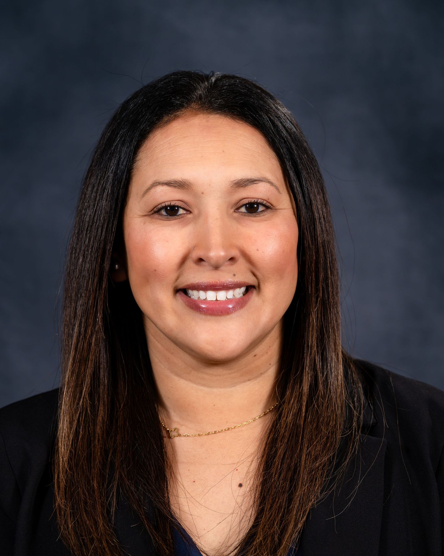 Professional headshot portrait of a woman with long dark hair and a warm smile against a dark background.