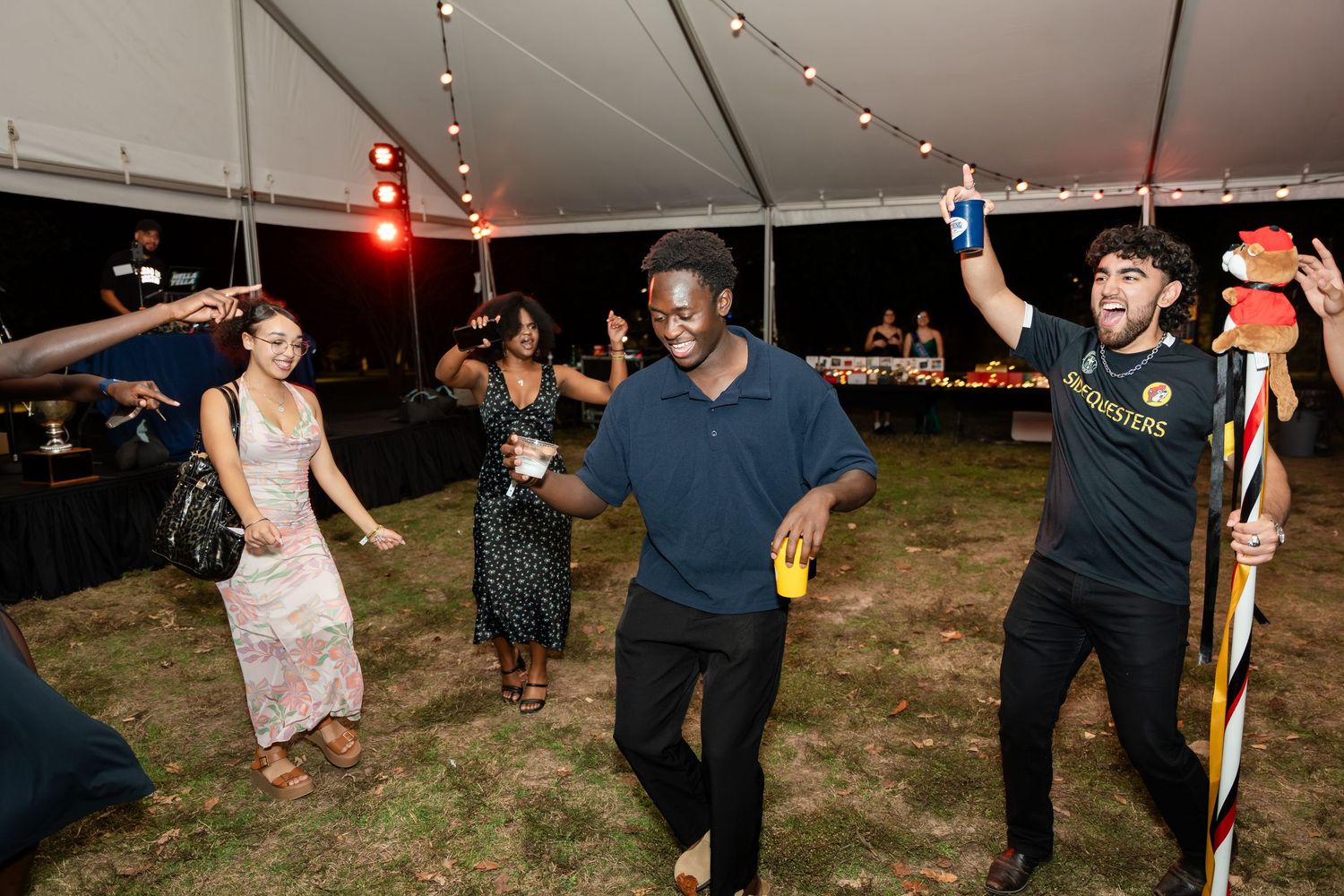 People dancing together outdoors at night during a festive celebration with string lights overhead.