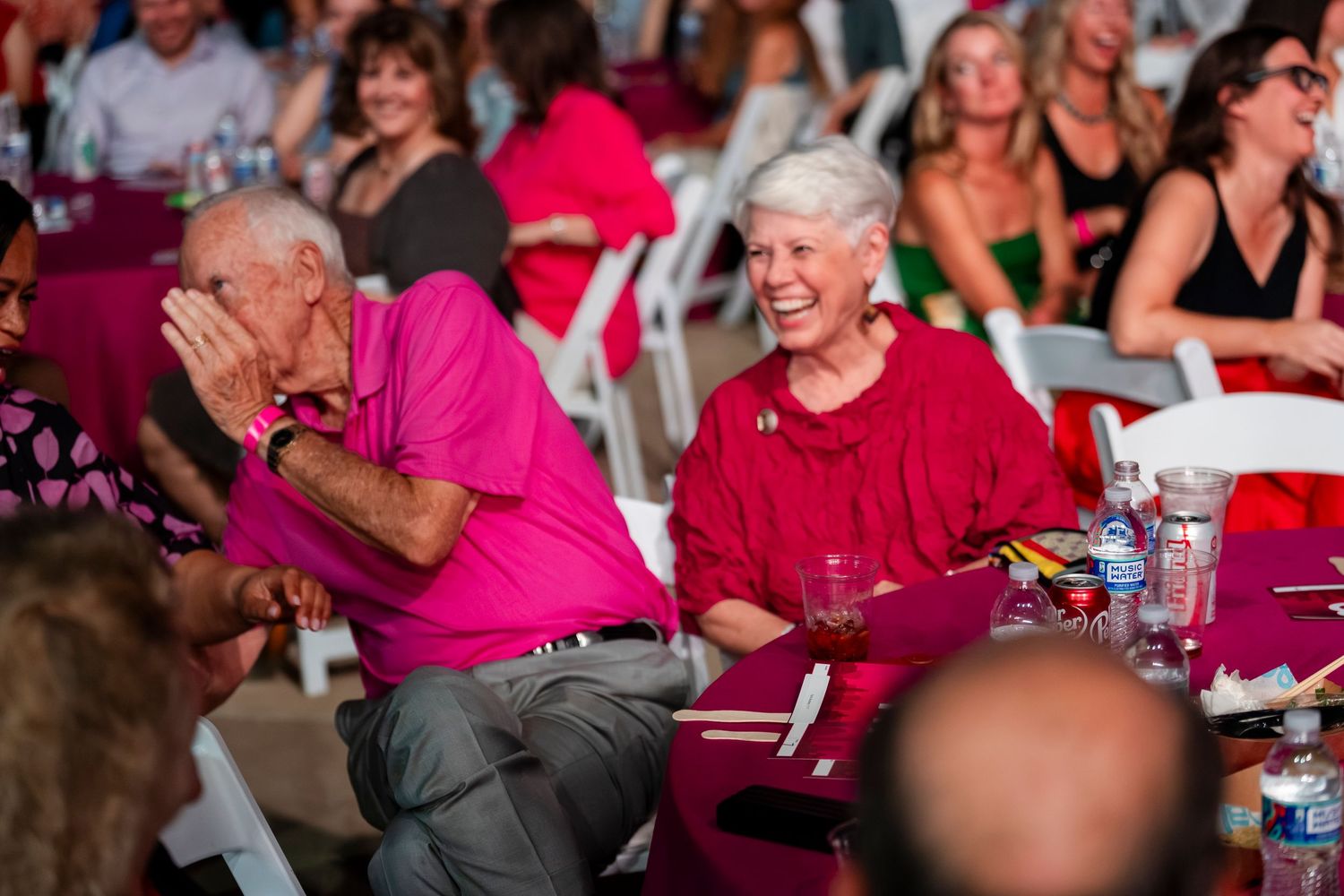 A group of people wearing pink shirts gather at tables during what appears to be a social event or celebration.