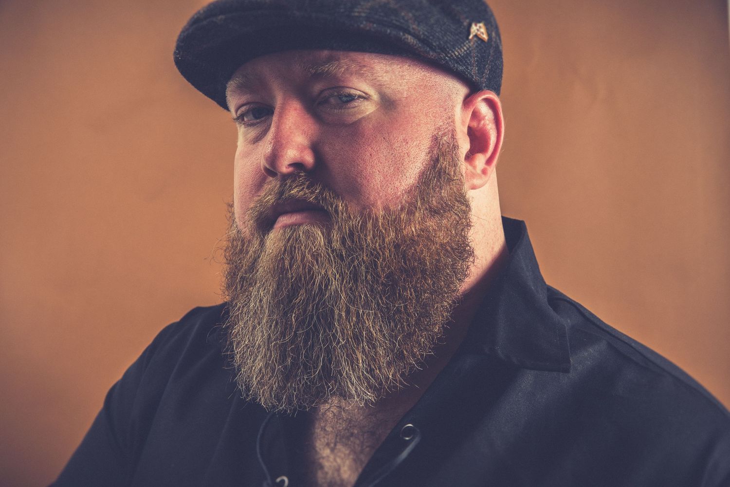 A series of profile photos showing a bearded person wearing a black cap against a warm brown background.