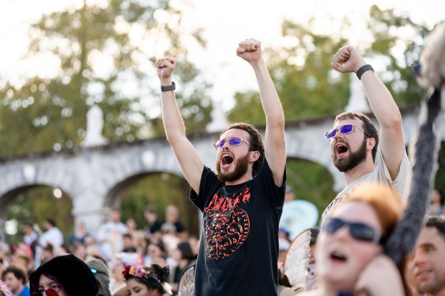 Energetic concert crowd with raised arms cheers and celebrates during an outdoor music festival performance.
