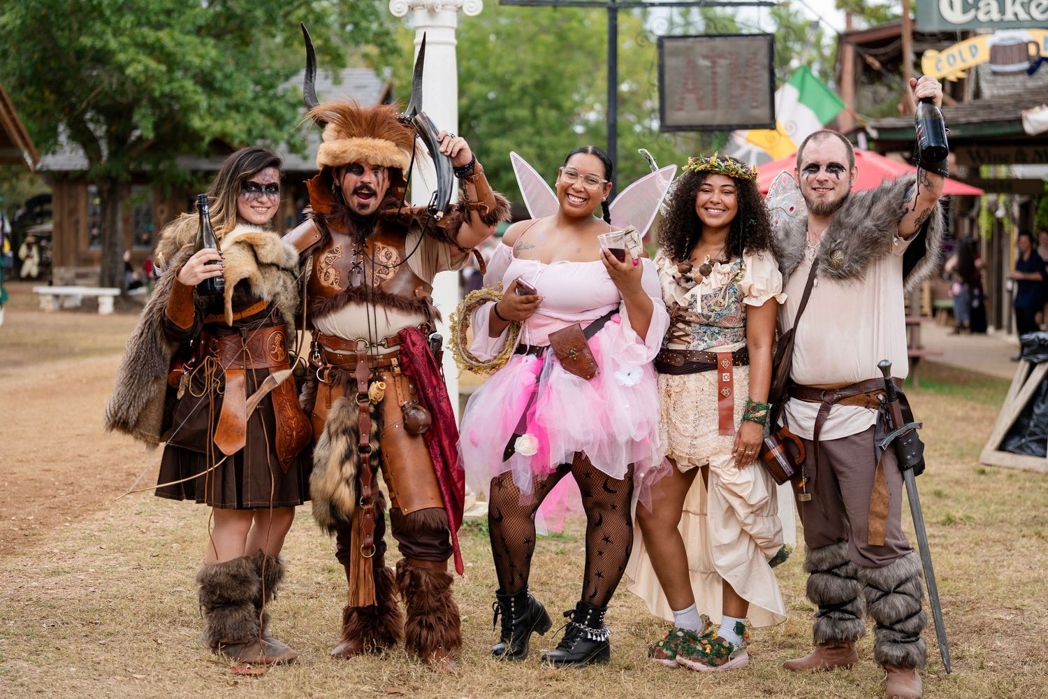 A group of people in medieval and fantasy costumes pose together at an outdoor festival or renaissance faire event.