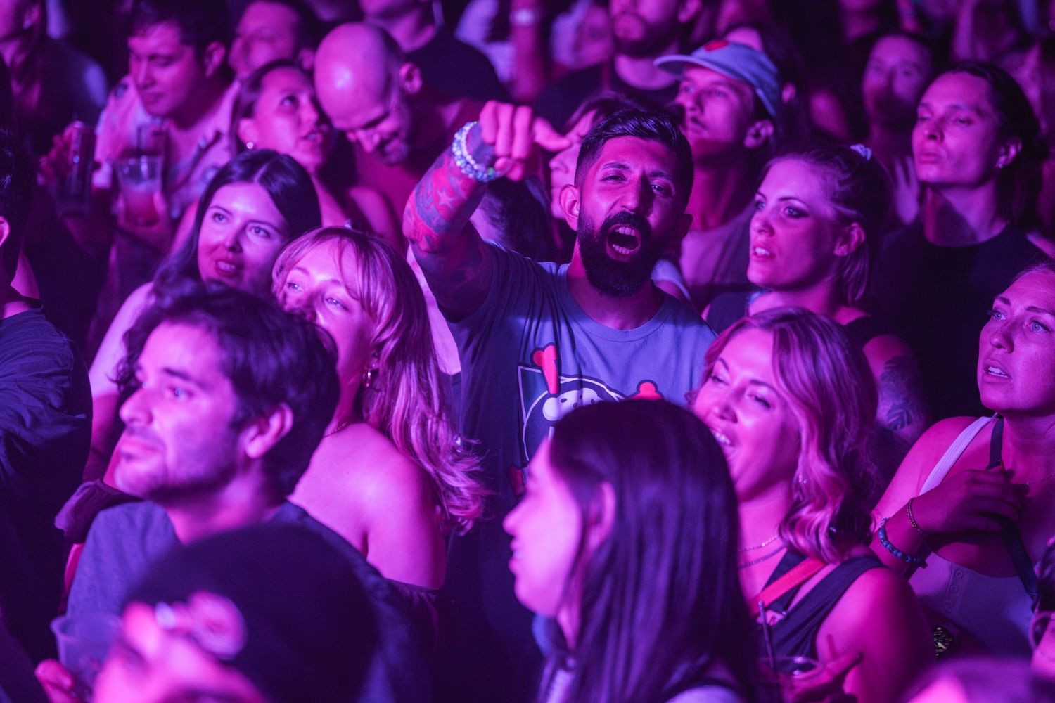 Concert audience illuminated by purple stage lighting watches performance with engaged expressions.