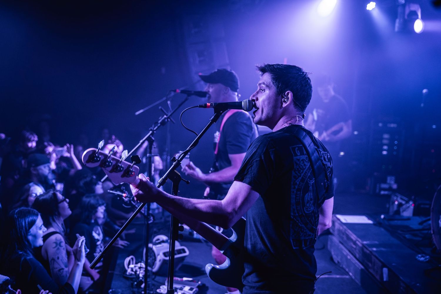 Performer singing and playing guitar on stage at concert venue with purple lighting and energetic crowd in foreground.