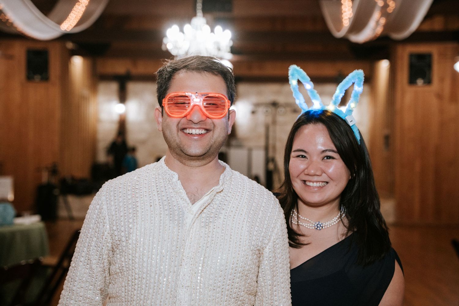 A festive party scene with guests wearing bunny ears and sunglasses in a wood-paneled venue.
