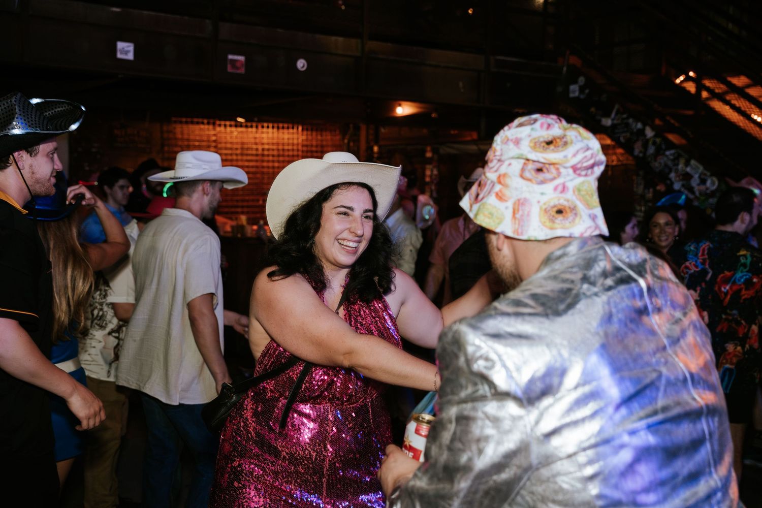 People dancing together at a festive party with colorful outfits and cowboy hats.
