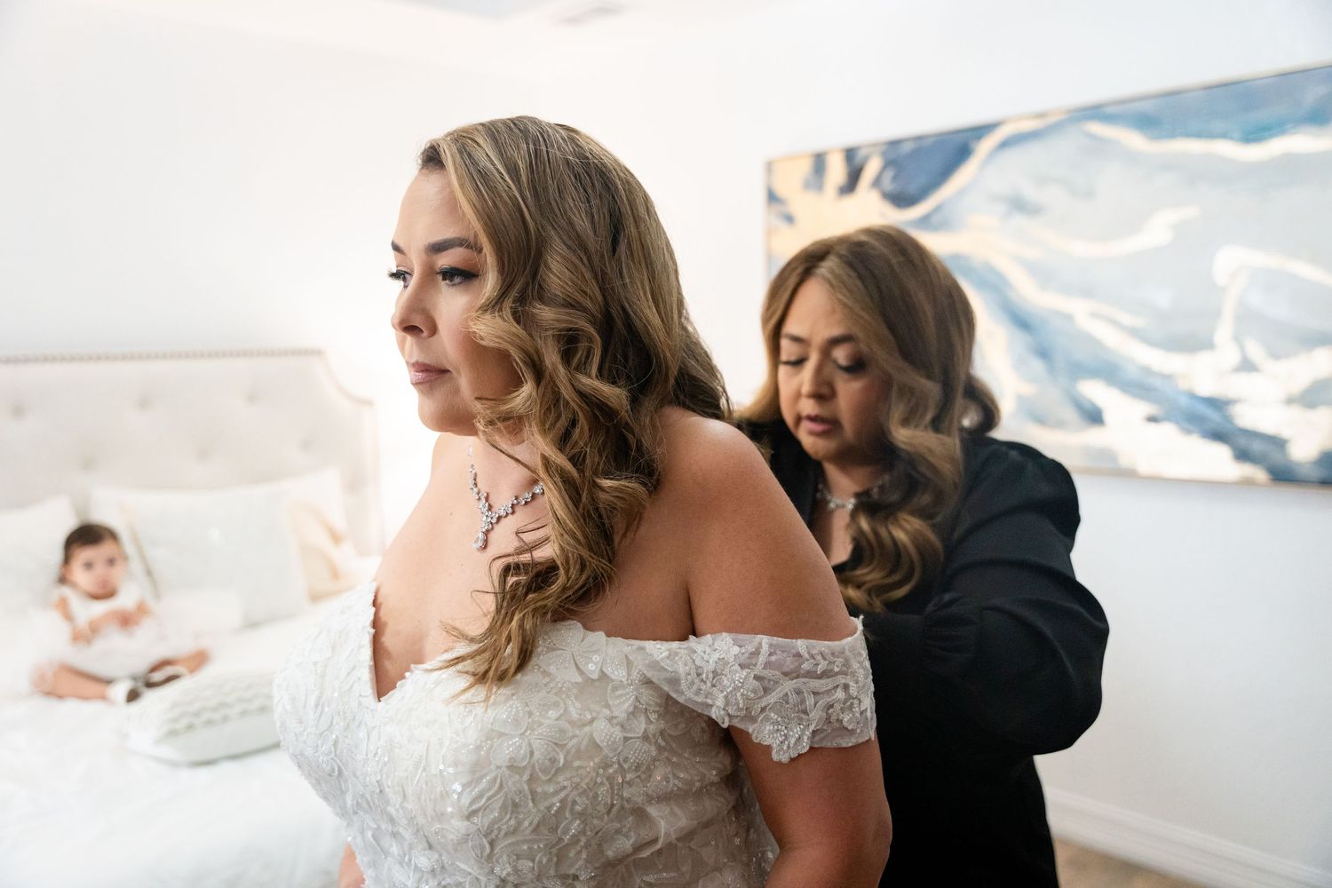 Final touches being made to the wedding dress in a bright room with a scenic backdrop.