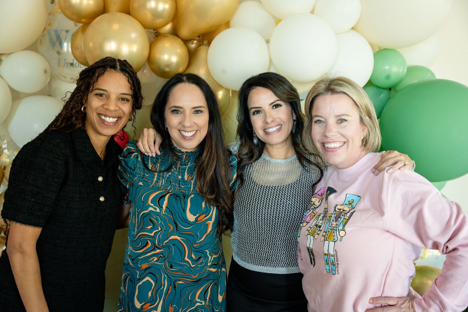 Group portrait in front of decorative balloon wall at special event.
